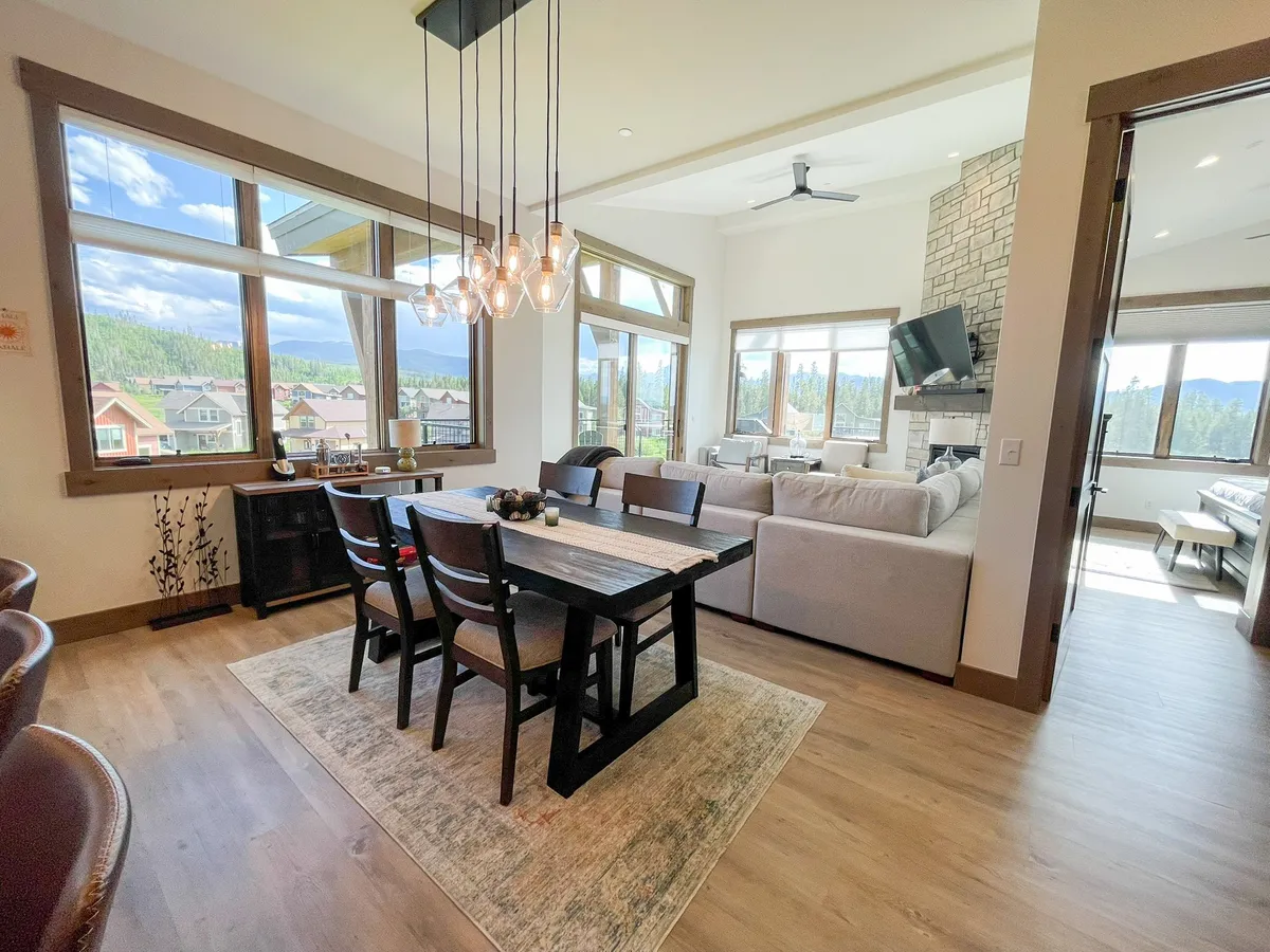 An inviting dining area with a large table set for a group, a comfortable sofa nearby, and expansive windows providing abundant natural light. The fireplace and elegant light fixture create a warm, social atmosphere.