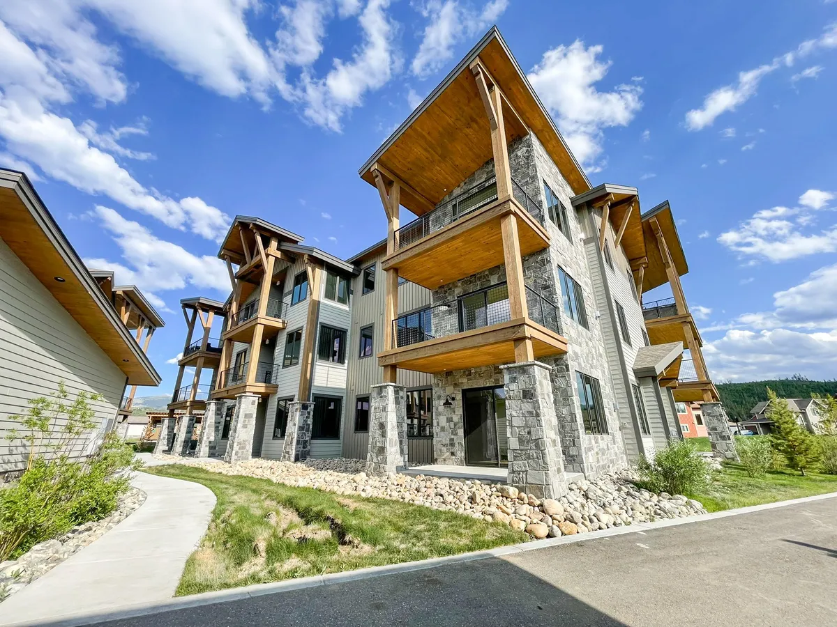 A wide-angle exterior view of the property reveals striking modern architecture, a natural stone facade, and expansive balconies overlooking lush greenery. The scene is bathed in natural light, highlighting the welcoming outdoor living spaces ideal for gatherings, relaxation, and enjoying scenic sunsets.