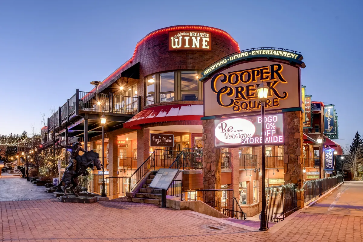 A vibrant exterior shot capturing the entrance to Cooper Creek Square, featuring lively signage, outdoor seating, and a distinctive horse sculpture. The area exudes a sense of community energy, with spaces for shopping, dining, and entertainment set against a backdrop of local art and culture.