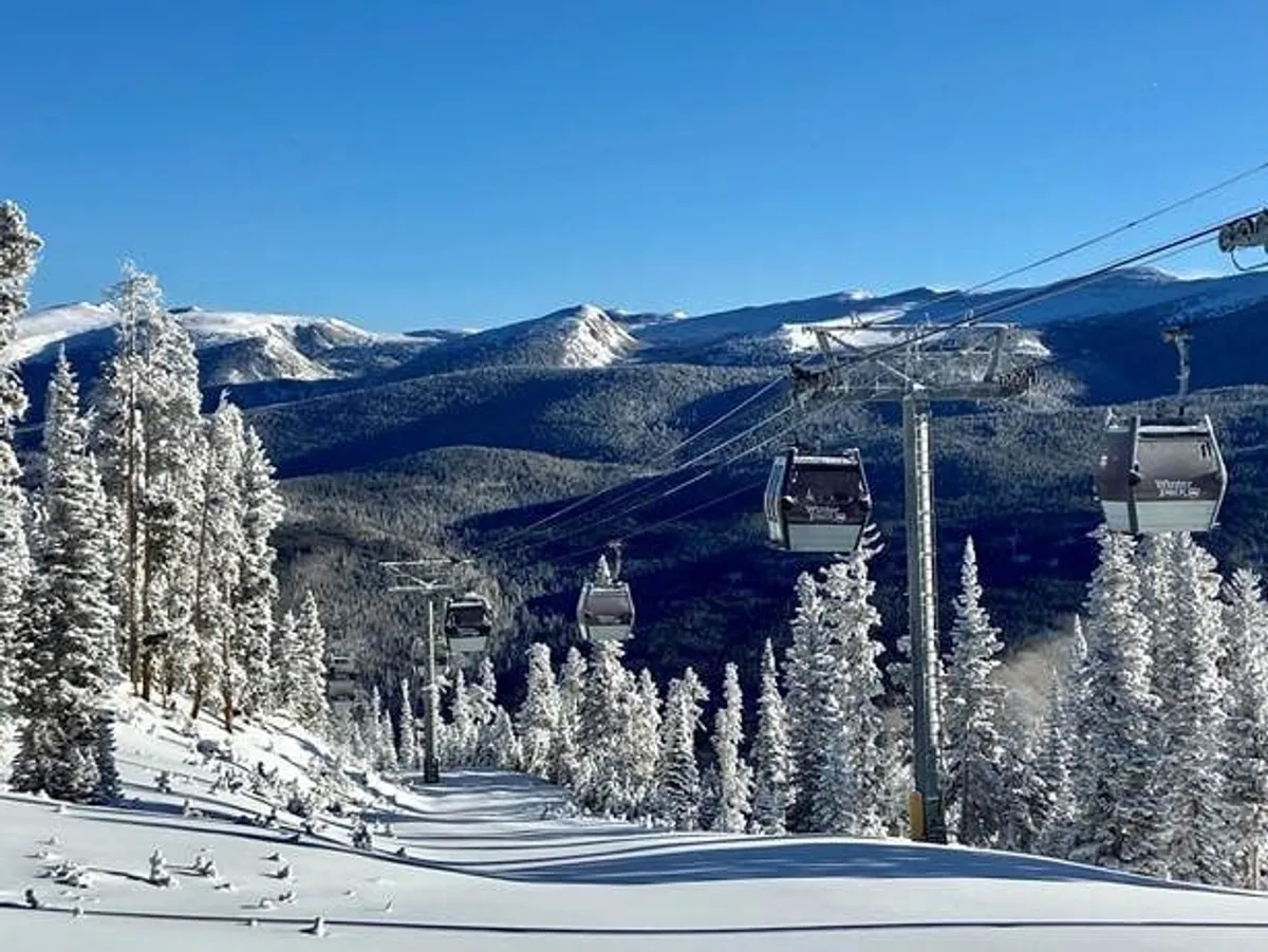 This image captures a scenic ski lift ascending over snow-covered trees with a sweeping mountain range in the background. The setting is iconic for winter sports, highlighting the natural beauty and adventure opportunities of the area.