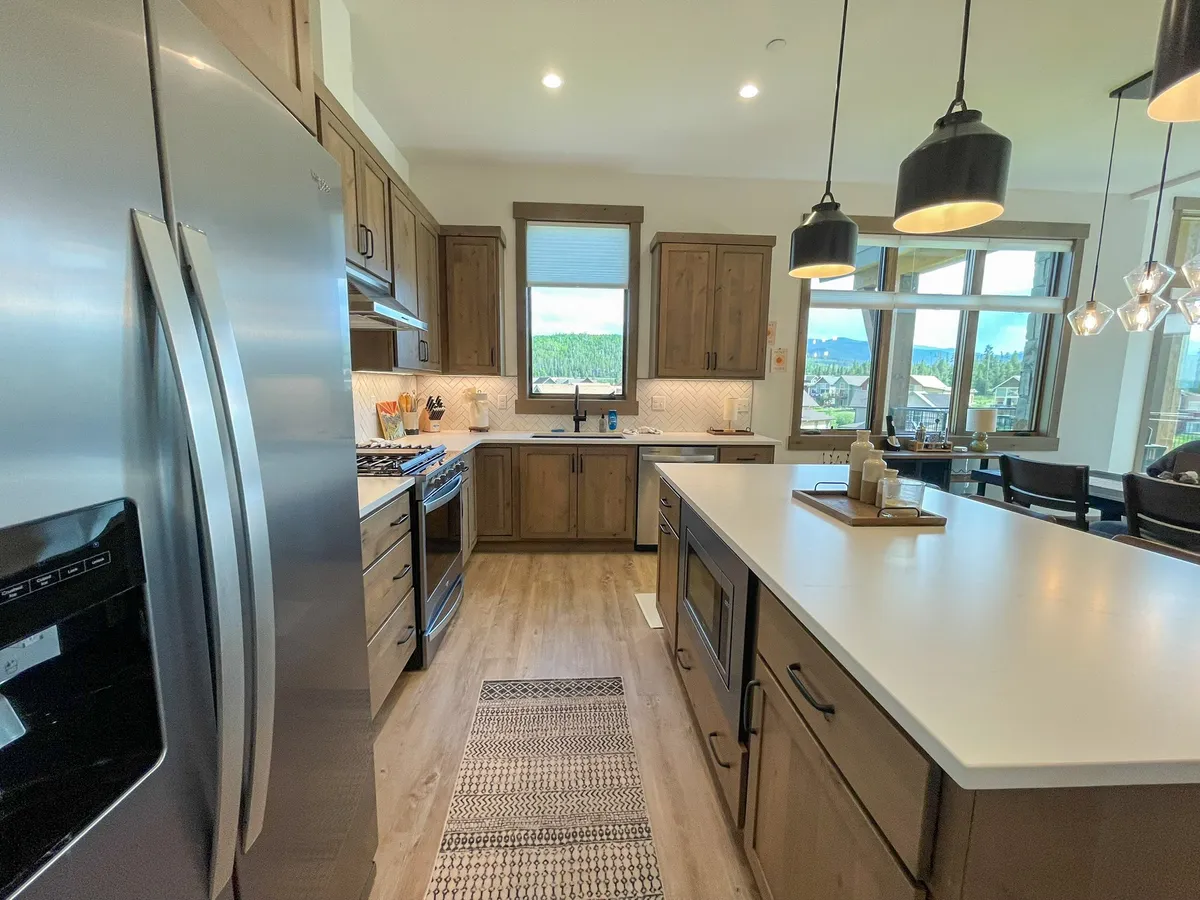 A modern kitchen with stainless steel appliances, wood cabinetry, a kitchen island with seating, and large windows that offer mountain views. The space feels welcoming and functional, ideal for shared cooking and meals.