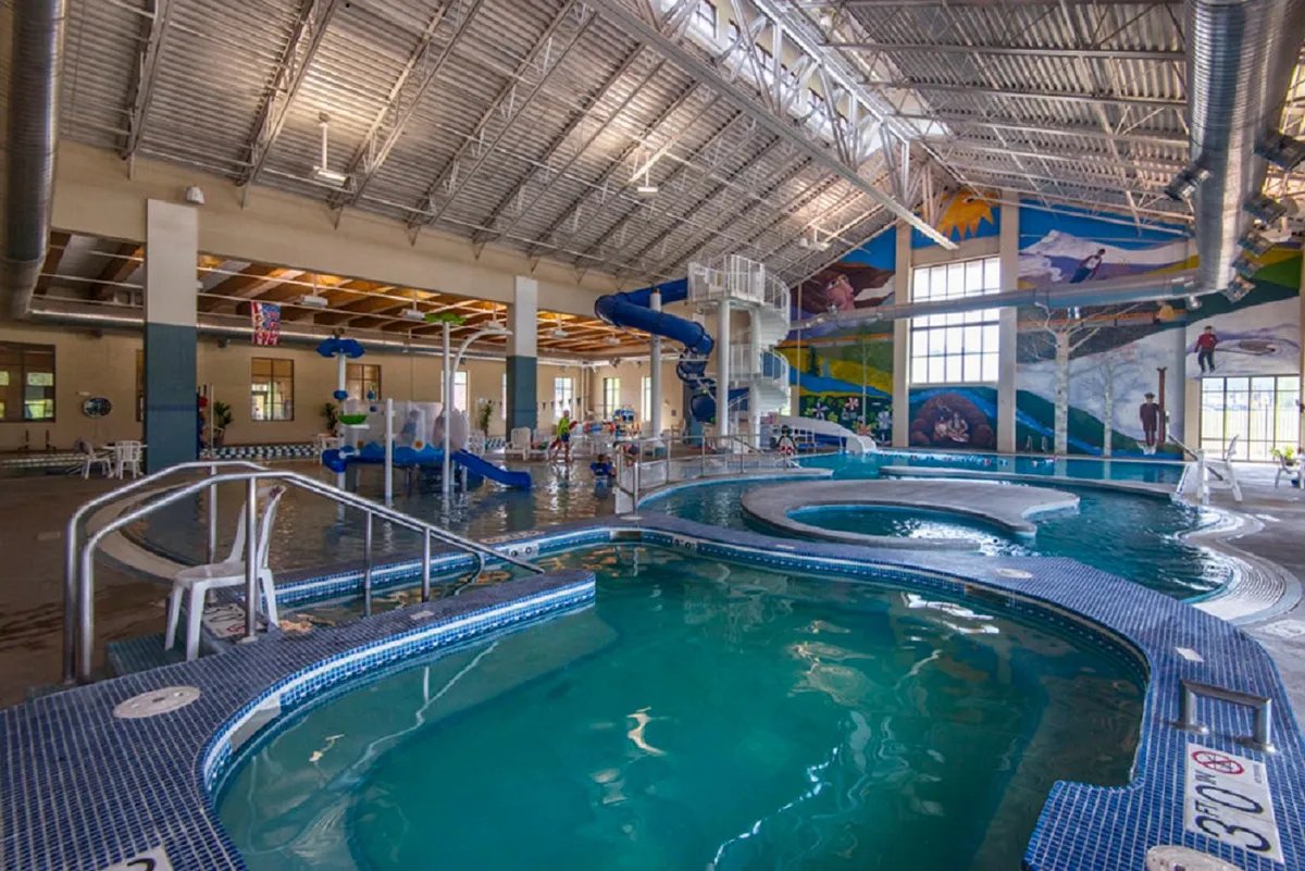 The vibrant interior of a recreation center with families and children enjoying colorful water slides and expansive pool areas. The playful atmosphere is enhanced by bright murals and the sound of laughter echoes in the air.