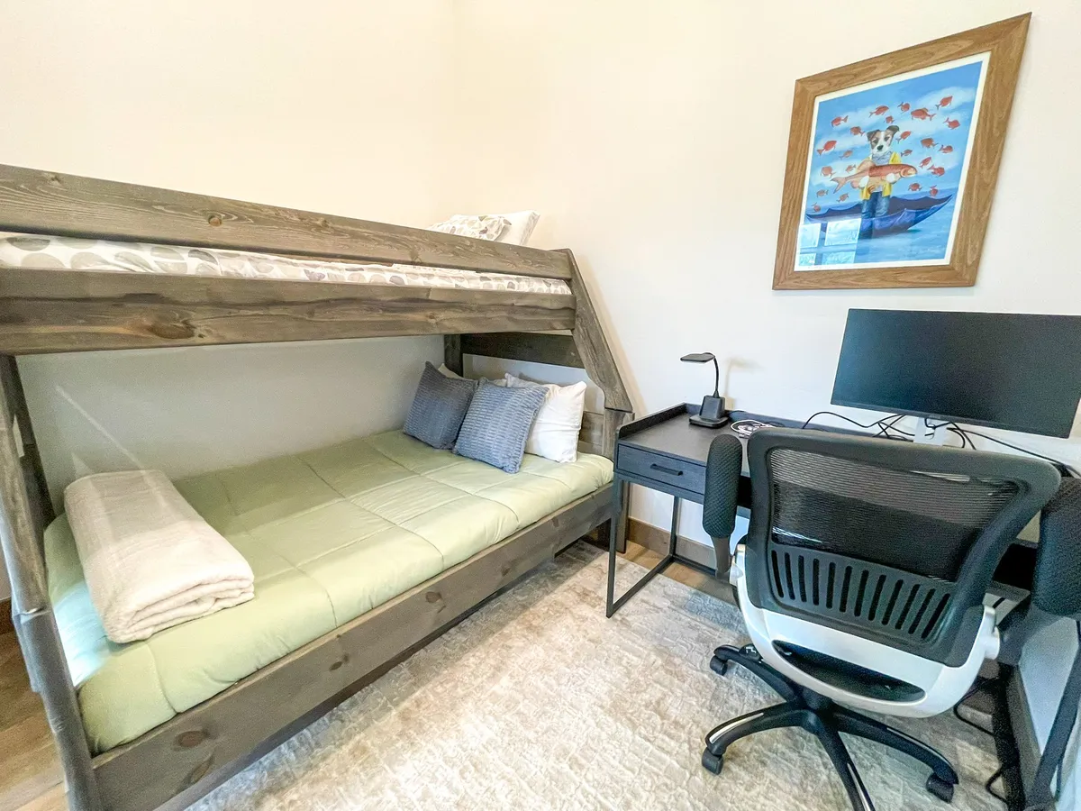 A playful yet practical bunk room featuring a twin-over-queen bunk bed, a functional desk with a computer, and cheerful décor. The space is designed to be both a fun retreat for kids or teens and a productive nook for work-from-home needs.