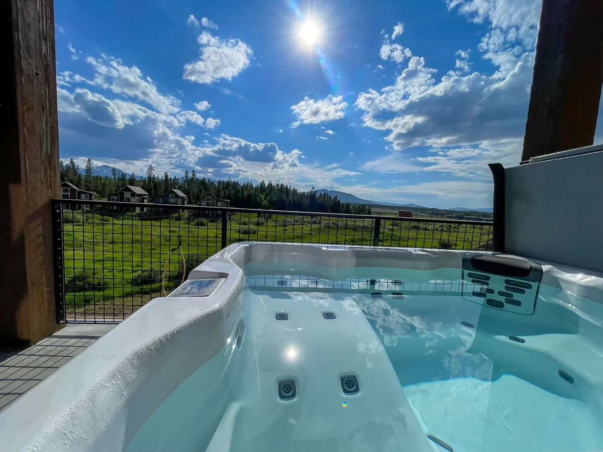 A tranquil exterior scene shows a private hot tub with expansive mountain views and a bright blue sky. The inviting setup emphasizes relaxation and luxury after an active day outdoors.