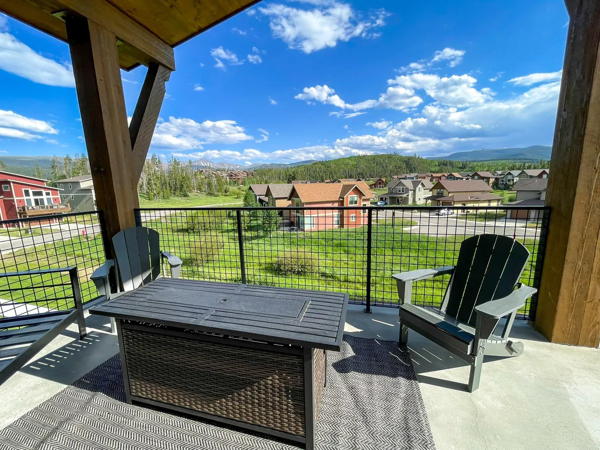 This image features a deck equipped with comfortable outdoor furniture, offering a direct and unobstructed mountain view. Neighboring houses are visible but do not detract from the peaceful, natural setting. The mood is tranquil, perfect for enjoying the scenery, socializing, or quietly reflecting with a cup of coffee.