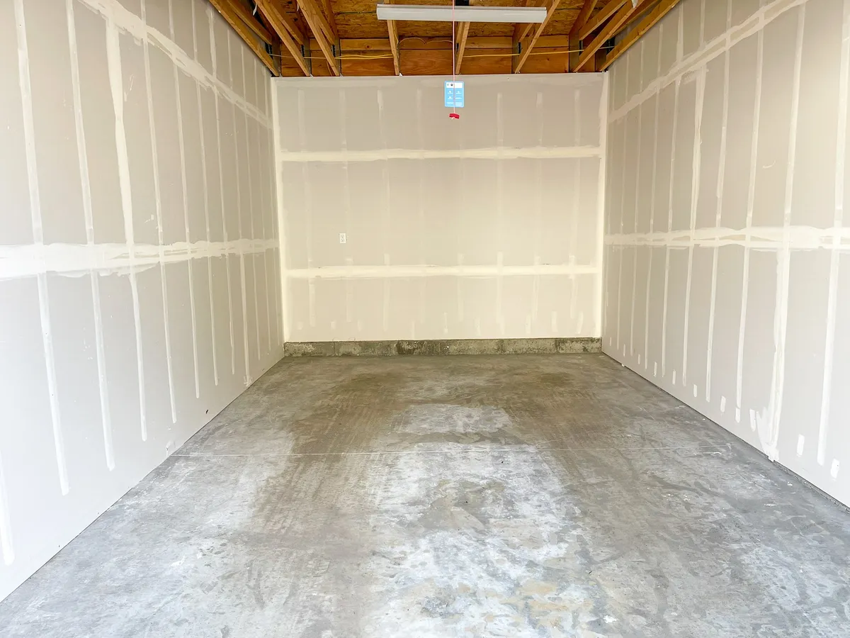 An interior view of a bare garage-like space featuring concrete floors, exposed ceilings, and unfinished walls. It emphasizes functionality and potential for gear storage, workspace, or organizing outdoor equipment as described in the content.